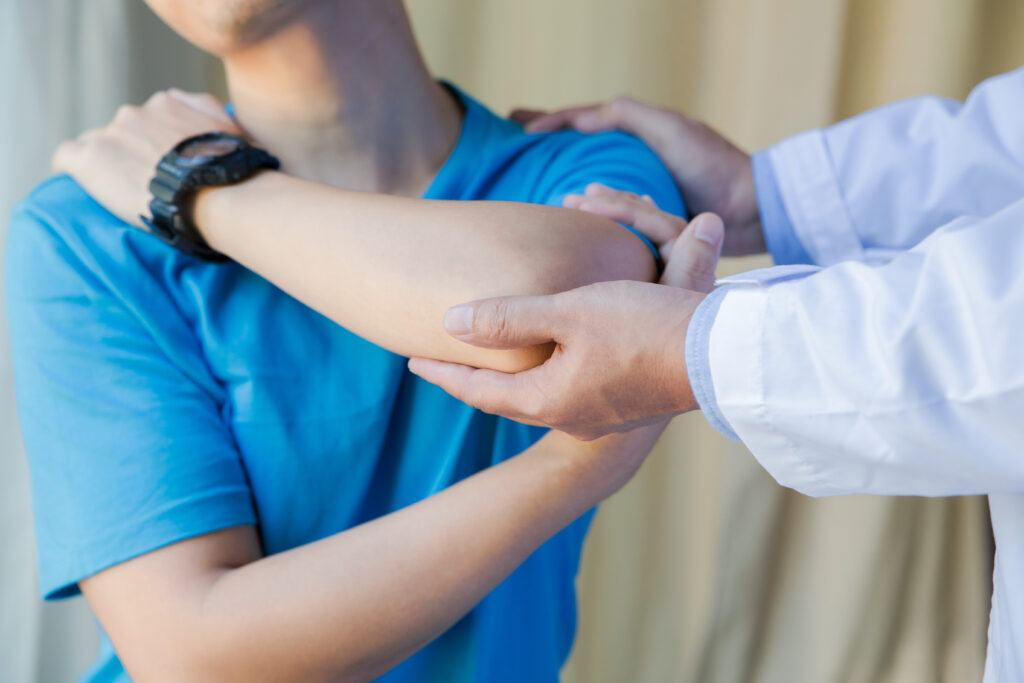 Un fisioterapista sta esaminando e manipolando delicatamente la spalla di un paziente. L'ambiente suggerisce una sessione professionale di fisioterapia della spalla.