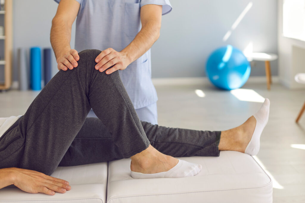 Fisioterapista in azione durante una sessione di fisioterapia al ginocchio, aiutando un paziente a migliorare la mobilità dell'articolazione in uno studio fisioterapico con attrezzature specializzate sullo sfondo.