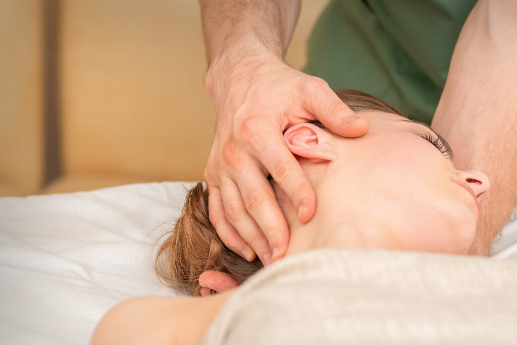 Fisioterapista in un centro di fisioterapia esegue un trattamento utilizzando tecniche manuali sulla testa di una paziente, per garantire rilassamento e cura.