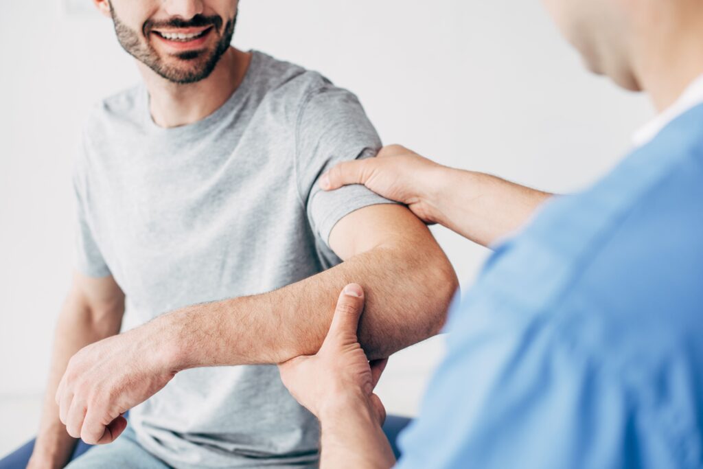 Un fisioterapista professionista sta eseguendo una seduta di riabilitazione per la periartrite alla spalla su un paziente. Il terapista sta delicatamente mobilizzando l'articolazione della spalla del paziente per alleviarne il dolore e migliorarne la mobilità.