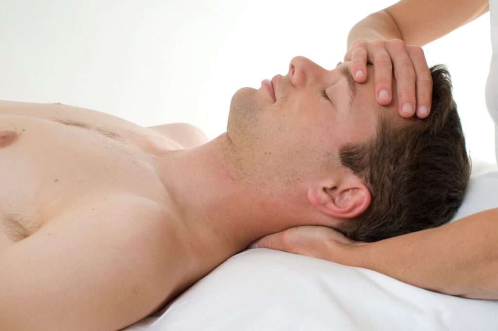 Un uomo è disteso su un lettino di fisioterapia mentre un fisioterapista applica una pressione delicata sulla fronte. Questo intervento potrebbe essere parte di un trattamento per le cause di mal di testa, dove il terapista utilizza tecniche di manipolazione cranica per alleviare la tensione e migliorare il flusso sanguigno, elementi spesso associati con diversi tipi di cefalea.
