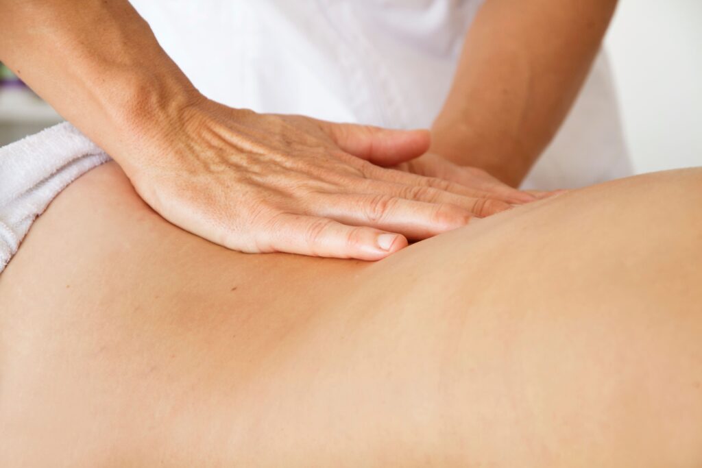 Un fisioterapista sta eseguendo un massaggio terapeutico su un paziente con mal di schiena basso. Le mani del terapista sono posizionate con cura sulla parte bassa della schiena del paziente, applicando una pressione mirata per alleviare tensione e dolore. Il trattamento è focalizzato sulla riduzione del disagio lombare attraverso la fisioterapia.